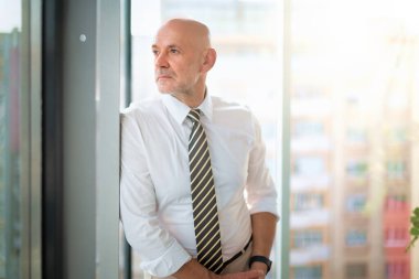 Ofiste duran orta yaşlı bir işadamı düşünceli görünüyor. Gömlek ve kravat takan kendinden emin profesyonel bir adam.. 