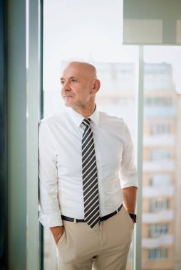 Ofiste duran orta yaşlı bir işadamı düşünceli görünüyor. Gömlek ve kravat takan kendinden emin profesyonel bir adam.. 