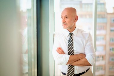 Ofiste duran orta yaşlı bir işadamı düşünceli görünüyor. Gömlek ve kravat takan kendinden emin profesyonel bir adam.. 