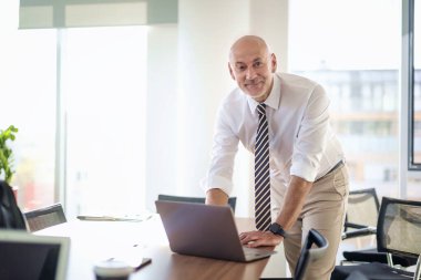 Orta yaşlı bir iş adamının ofis masasında dizüstü bilgisayar kullanırken görüntüsü. Modern bir ofiste çalışan profesyonel bir adam..