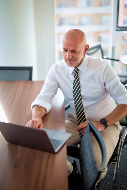 Orta yaşlı bir iş adamının ofis masasında dizüstü bilgisayar kullanırken görüntüsü. Modern bir ofiste çalışan profesyonel bir adam..