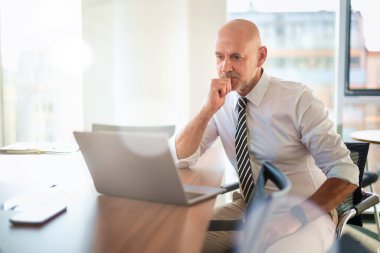 Orta yaşlı bir iş adamının ofis masasında dizüstü bilgisayar kullanırken görüntüsü. Modern bir ofiste çalışan profesyonel bir adam..