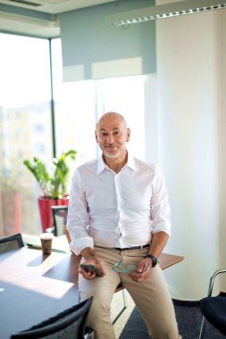 Ofiste cep telefonu kullanan orta yaşlı bir profesyonel. Kendine güvenen işadamı parlak bir ofiste duruyor ve mesajlaşıyor..