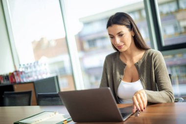 İş için bilgisayarını kullanan gülümseyen bir iş kadını. Modern bir ofiste oturan çekici, profesyonel bir kadın web konferansı yapıyor..