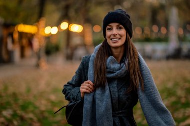 Bir sonbahar günü şehir parkında yürüyen orta yaşlı güzel bir kadın. Gülümseyen kadın ceketli ve bereli..