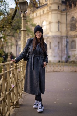 Bir sonbahar günü şehir parkında yürüyen orta yaşlı güzel bir kadın. Gülümseyen kadın ceketli ve bereli..