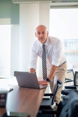 Orta yaşlı işadamı ofisinde masasında duruyor ve bir not defteri kullanıyor. İş kıyafeti giyen profesyonel bir erkek..