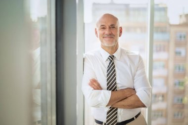 Ofiste dikilip kameraya bakan orta yaşlı bir işadamı. Gömlek ve kravat takan kendine güvenen profesyonel bir adam.. 