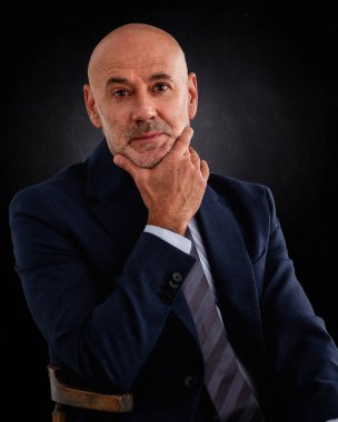 Beyaz adam takım elbise giyiyor ve izole edilmiş siyah arka planda oturuyor. Uzayı kopyala Eller çenede..