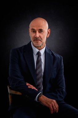 Beyaz adam takım elbise giyiyor ve izole edilmiş siyah arka planda oturuyor. Boşluğu kopyala. 