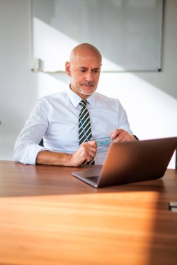 Orta yaşlı bir iş adamının ofis masasında dizüstü bilgisayar kullanırken görüntüsü. Modern bir ofiste çalışan profesyonel bir adam..