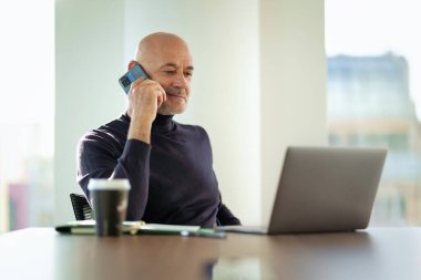 Kafkas işadamı ofis masasında oturuyor ve cep telefonu ve not defteri kullanıyor. Modern bir ofiste çalışan profesyonel bir erkek.. 