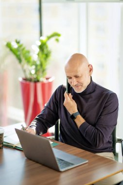 Kafkas işadamı ofis masasında oturuyor ve cep telefonu ve not defteri kullanıyor. Modern bir ofiste çalışan profesyonel bir erkek.. 