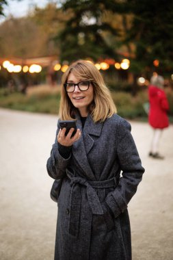 Dışarı çıkıp işten sonra akıllı telefon kullanan mutlu bir kadının portresi. Sarı saçlı, sıradan kıyafetler giyen bir kadın.. 