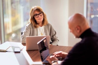 İş için bilgisayarını kullanan gülümseyen bir iş kadını. Çekici profesyonel kadın iş kıyafeti giyiyor ve modern bir ofiste oturuyor.. 