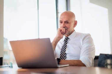 Bilgisayarını kullanarak orta yaşlı bir iş adamı olduğunu düşünüyor. Modern bir ofiste çalışan ve internet konferansı yapan profesyonel bir erkek..