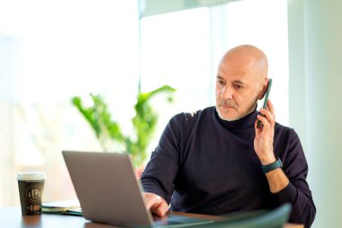 Kafkas işadamı ofis masasında oturuyor ve cep telefonu ve not defteri kullanıyor. Modern bir ofiste çalışan profesyonel bir erkek.. 