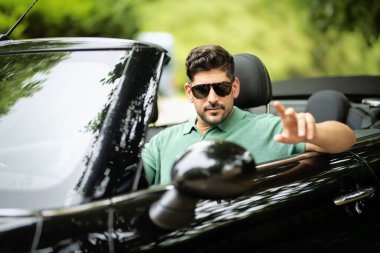 Güneş gözlüğü takan, üstü açık bir arabada oturan ve yolda araba süren yakışıklı bir adam.. 