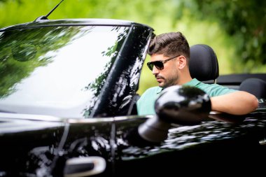 Güneş gözlüğü takan, üstü açık bir arabada oturan ve yolda araba süren yakışıklı bir adam.. 