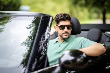 Güneş gözlüğü takan, üstü açık bir arabada oturan ve yolda araba süren yakışıklı bir adam.. 