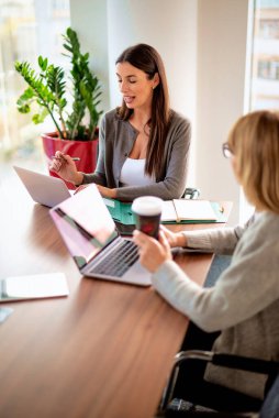 Modern bir ofiste masa başında oturan ve dizüstü bilgisayarlarla çalışan iki iş kadını. Takım çalışması. Bir grup iş adamı toplantı sırasında tartışıyor.