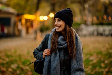 Bir sonbahar günü şehir parkında yürüyen orta yaşlı güzel bir kadın. Beyaz kadın ceketli ve bereli..