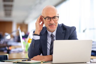 Ofiste oturan kıdemli işadamı. Profesyonel erkek iş için dizüstü bilgisayar kullanıyor ve internet konferansı yapıyor.. 