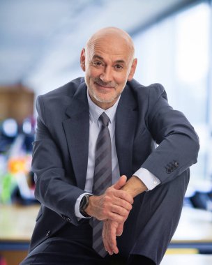 Ofiste oturan kıdemli işadamı. Profesyonel erkek giysisi giyip kameraya bakıyor.. 