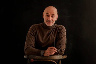 Karanlık bir arkaplanda oturan son sınıf öğrencisi. Kendine güvenen erkek kazak giyiyor. İzole edilmiş arka plan. Boşluğu kopyala. 