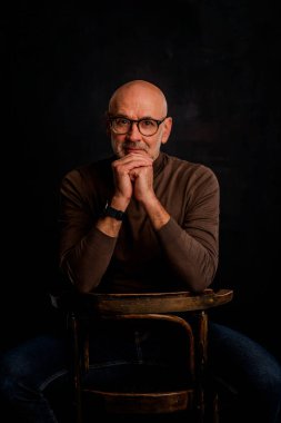 Karanlık bir arkaplanda oturan son sınıf öğrencisi. Kendine güvenen erkek kazak giyiyor. İzole edilmiş arka plan. Boşluğu kopyala. 