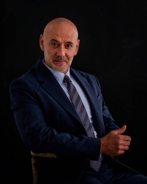 Takım elbiseli ve izole edilmiş siyah arka planda oturan beyaz bir adam. Uzayı kopyala Son sınıf öğrencisi çok düşünceli görünüyor.. 