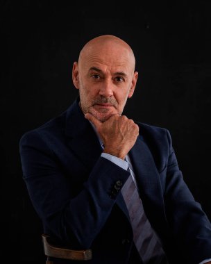 Takım elbiseli ve izole edilmiş siyah arka planda oturan beyaz bir adam. Uzayı kopyala Son sınıf öğrencisi çok düşünceli görünüyor.. 