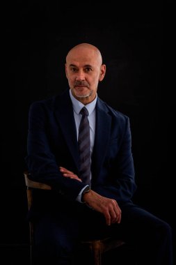 Takım elbiseli ve izole edilmiş siyah arka planda oturan beyaz bir adam. Uzayı kopyala Son sınıf öğrencisi çok düşünceli görünüyor.. 