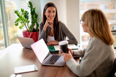 Modern bir ofiste masa başında oturan ve dizüstü bilgisayarlarla çalışan iki iş kadını. Takım çalışması. Bir grup iş adamı toplantı sırasında tartışıyor.