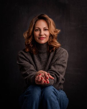 Gülümseyen olgun bir kadının portresi. Esmer, kendine güvenen bir kadın. Balıkçı yaka kazak giyen çekici bir kadın. Boşluğu kopyala. 