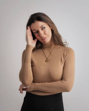 Esmer kadın izole edilmiş arka planda duruyor. Balıkçı yaka kazak giyen ve düşünceli görünen çekici bir kadın. Uzayı kopyala Elleriyle dokunuyor.. 