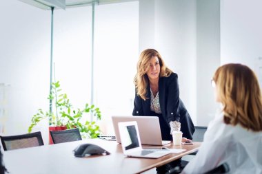 Bir grup iş kadını masamda oturup fikirlerini sunarken dizüstü bilgisayar kullanıyor. Modern bir ofiste takım çalışması..