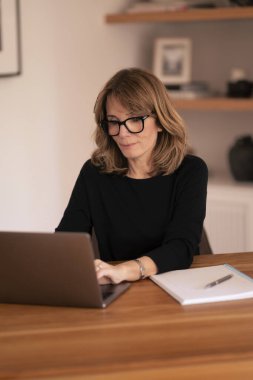 Evde dizüstü bilgisayarının önünde oturan ve video konferansı yapan sarışın bir kadın. Evden çalışan orta yaşlı beyaz bir kadın. Merkez Ofis. 