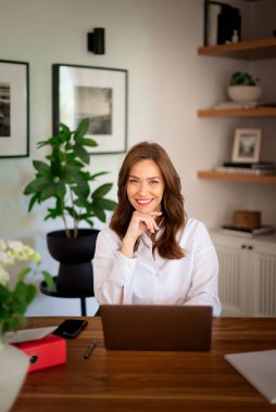 Esmer saçlı kadın masada oturuyor ve defterini kullanıyor. Evden çalışan kendine güvenen bir iş kadını. Merkez Ofis.