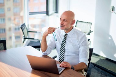 Orta yaşlı bir iş adamının ofis masasında dizüstü bilgisayar kullanırken görüntüsü. Modern bir ofiste çalışan profesyonel bir adam..