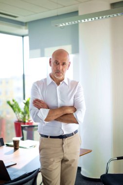 Modern bir ofiste masasında duran orta yaşlı bir iş adamı. Profesyonel bir adam sıradan giyiniyor ve düşünceli görünüyor.. 