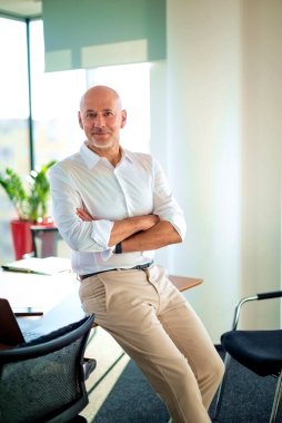 Modern bir ofiste masasında duran orta yaşlı bir iş adamı. İş kıyafeti giyen profesyonel bir adam.. 