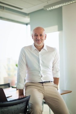 Modern bir ofiste masasında duran orta yaşlı bir iş adamı. İş kıyafeti giyen profesyonel bir adam.. 