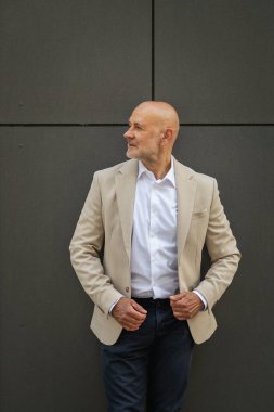 Gri bir duvarın önünde caddede duran orta yaşlı bir adam. İş kıyafeti giymiş yakışıklı bir iş adamı.. 