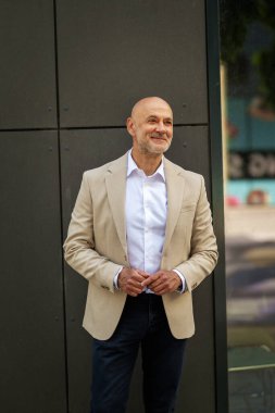 Gri bir duvarın önünde caddede duran orta yaşlı bir adam. İş kıyafeti giymiş yakışıklı bir iş adamı.. 
