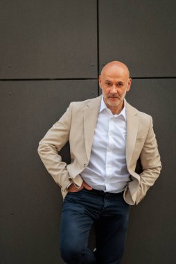Gri bir duvarın önünde caddede duran orta yaşlı bir adam. İş kıyafeti giymiş yakışıklı bir iş adamı.. 