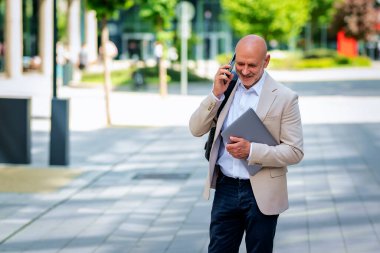 Yakışıklı bir adam dizüstü bilgisayar tutuyor ve şehirde finans sektöründe yürüyor. Orta yaşlı işadamı iş kıyafeti giyiyor ve telefon görüşmesi yapıyor.. 