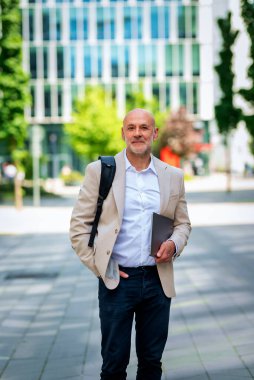 Yakışıklı bir adam dizüstü bilgisayar tutuyor ve şehirde finans sektöründe yürüyor. Orta yaşlı işadamı iş kıyafeti giyiyor.. 