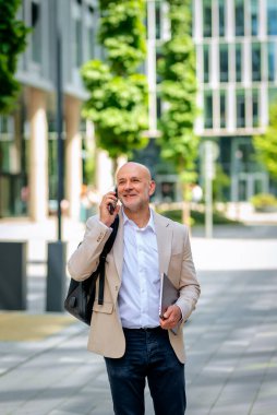 Yakışıklı bir adam dizüstü bilgisayar tutuyor ve şehirde finans sektöründe yürüyor. Orta yaşlı işadamı iş kıyafeti giyiyor ve telefon görüşmesi yapıyor.. 