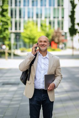 Yakışıklı bir adam dizüstü bilgisayar tutuyor ve şehirde finans sektöründe yürüyor. Orta yaşlı işadamı iş kıyafeti giyiyor ve telefon görüşmesi yapıyor.. 